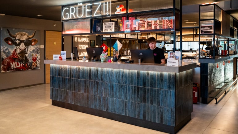 Rezeption in modernem Hotel mit Neonlichtern und Kuhbild an der Wand.