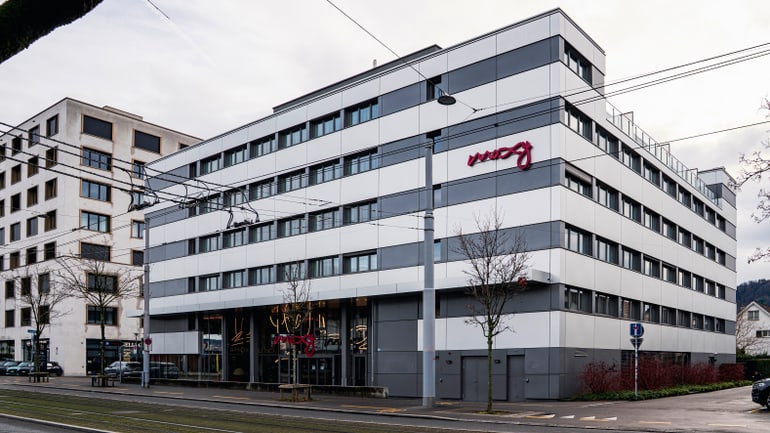 Modernes mehrstöckiges Gebäude mit Glasfassade und rotem Schriftzug.