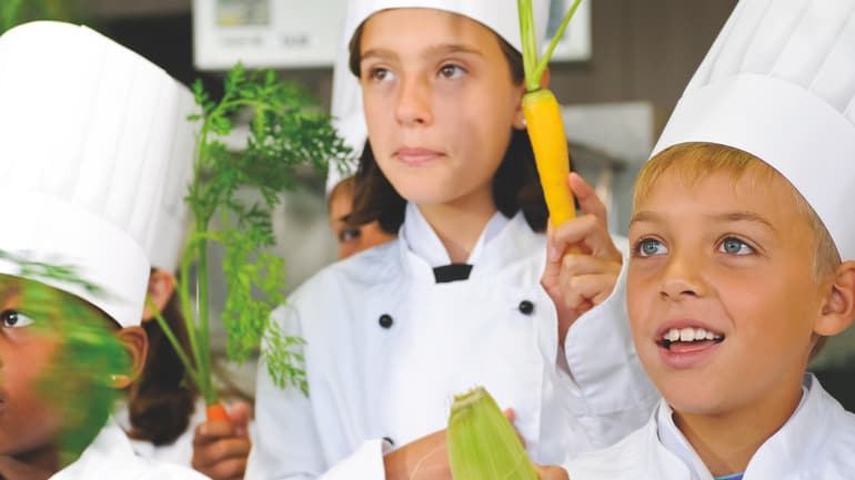 Kinder in Kochuniformen halten Gemüse.