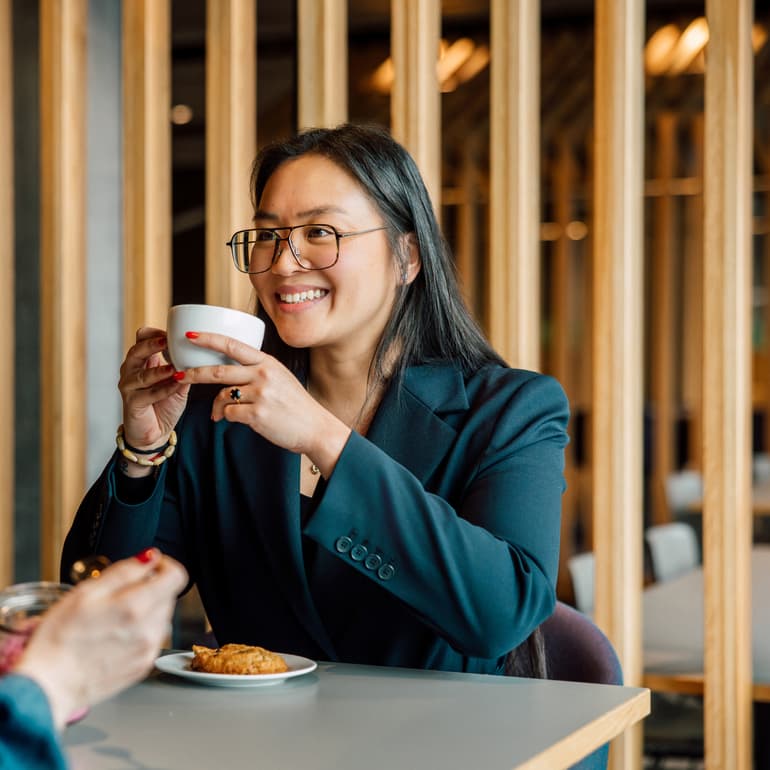 Frau im Café, trinkt aus einer Tasse und lächelt.