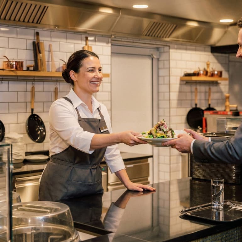 Frau serviert Mann einen Salat über die Theke in der Küche.