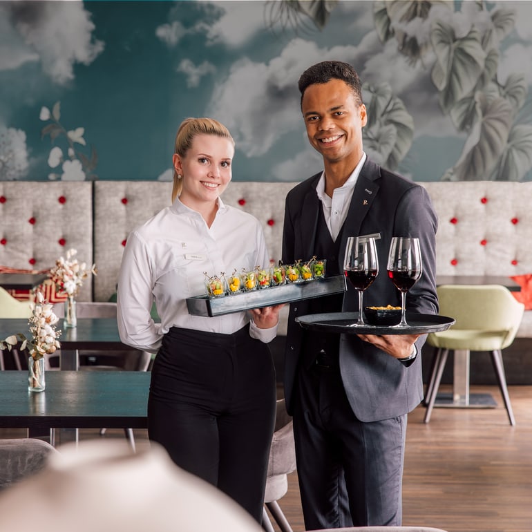 Zwei Kellner in einem stilvollen Restaurant mit Tabletts.",