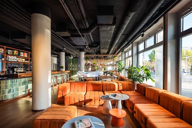 Modern lounge with orange sofas and large windows.