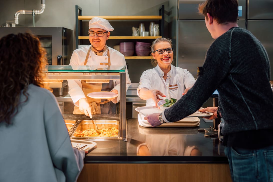 Küchenpersonal serviert Essen an Kunden in einem SV Restaurant.